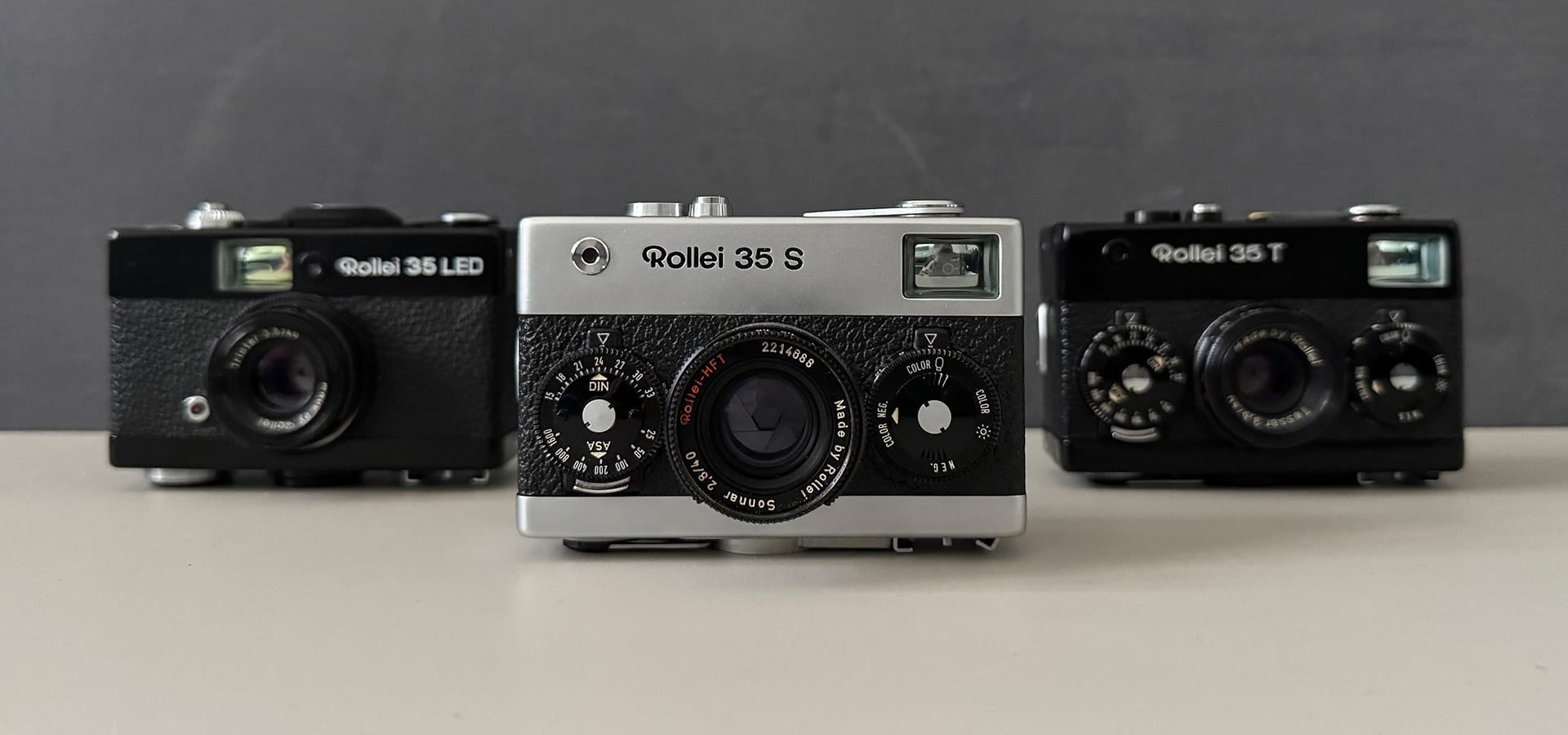 Sieben Minox 35 Kameras in einer Reihe vor einer blauen Wand.