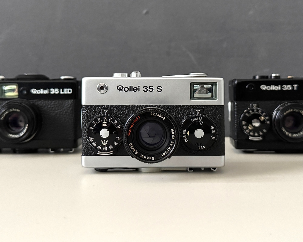 Sieben Minox 35 Kameras in einer Reihe vor einer blauen Wand.